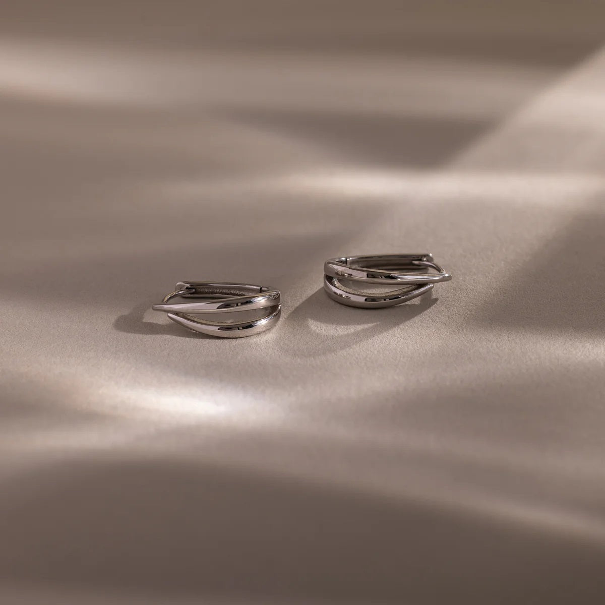 Pair of silver hoop earrings on a beige fabric background