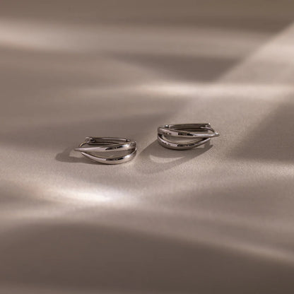 Pair of silver hoop earrings on a beige fabric background