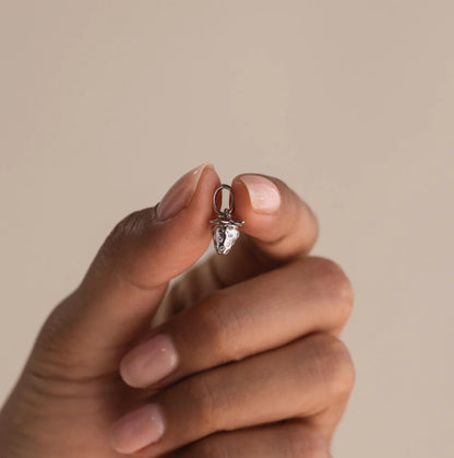 Hand holding a small silver ring with a clear gemstone against a beige background