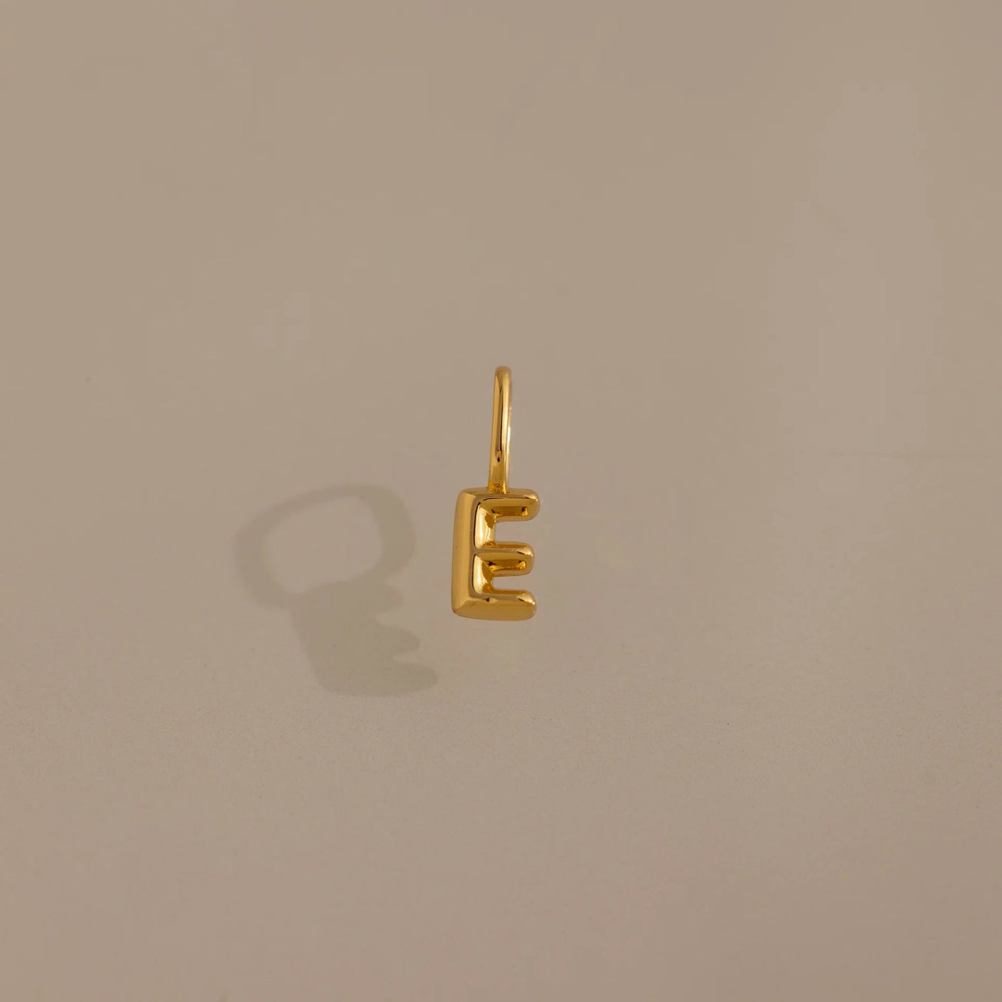 Gold letter 'E' charm on a beige background