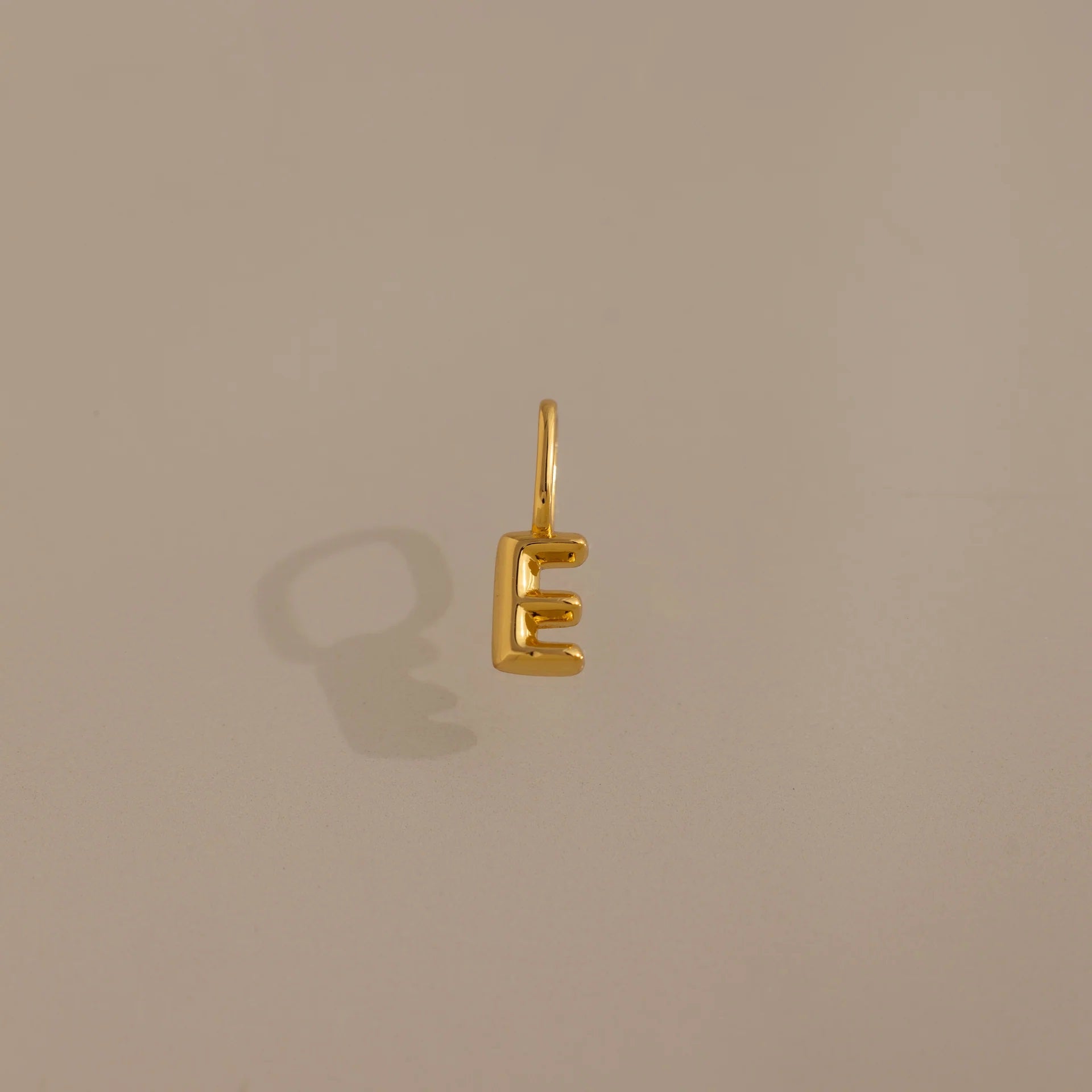 Gold letter 'E' charm on a beige background