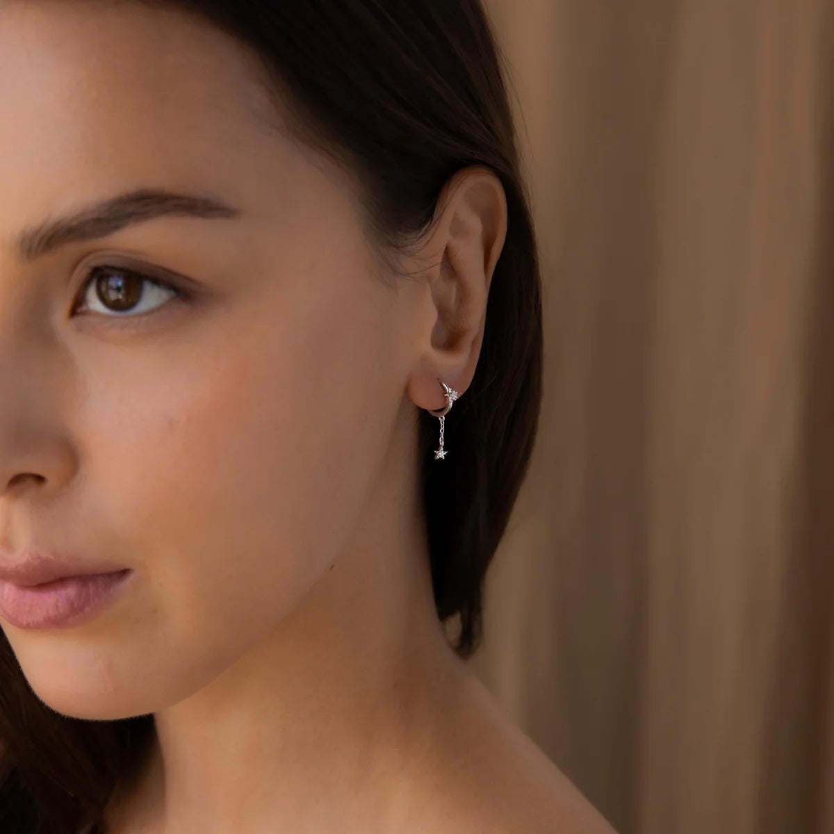 Close-up of a woman wearing a delicate silver earring against a neutral background