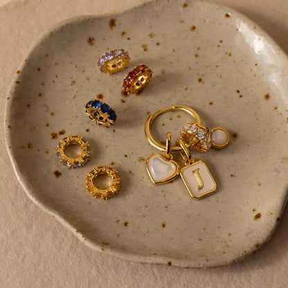 Gold earrings with various designs on a speckled ceramic dish.