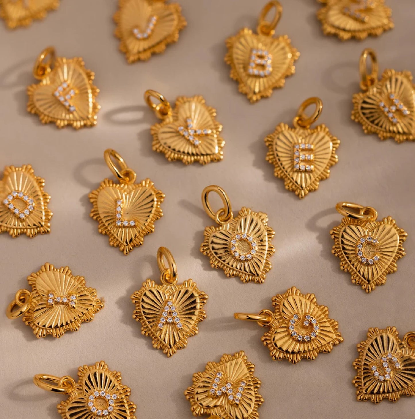 Gold heart-shaped pendants with letters on a beige background