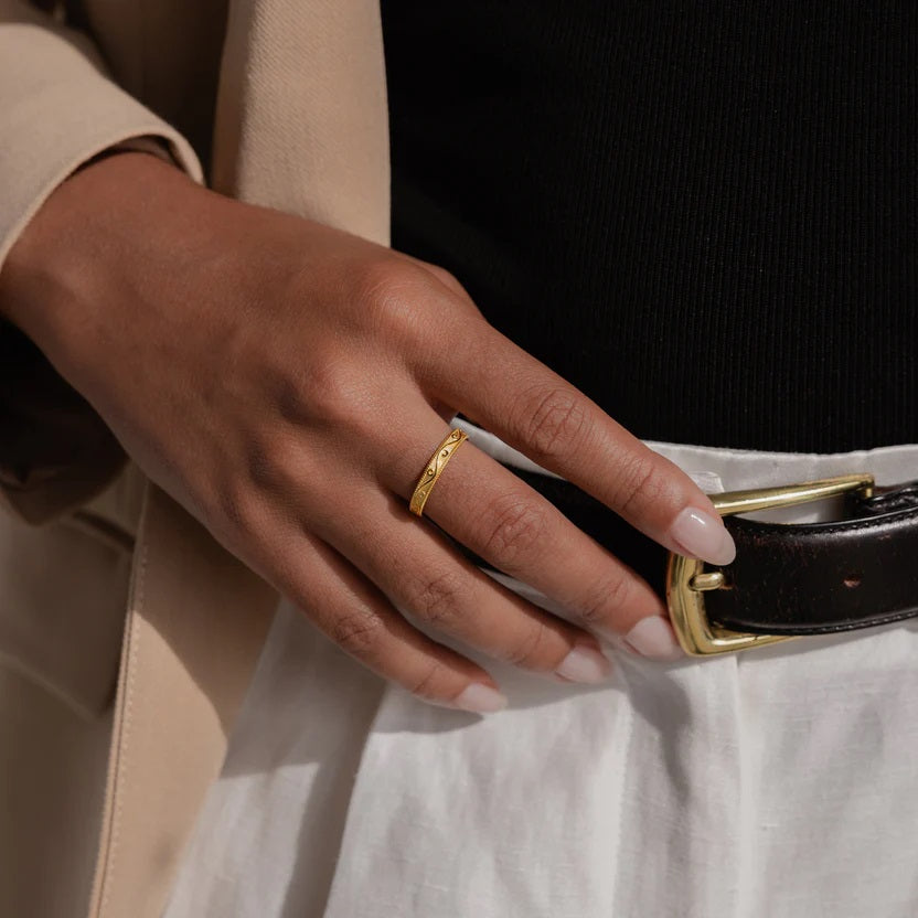 Hand wearing a gold ring on a black belt with a white shirt