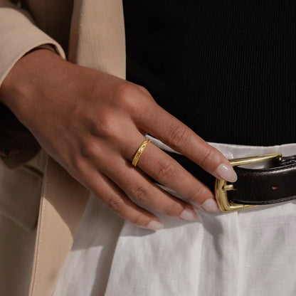 Hand wearing a gold ring on a black belt with a white shirt