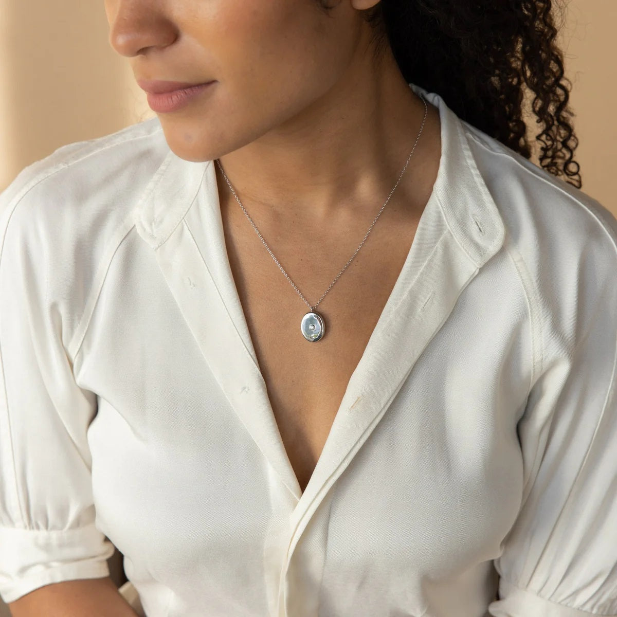 Woman wearing a necklace with a pendant, dressed in a white shirt.
