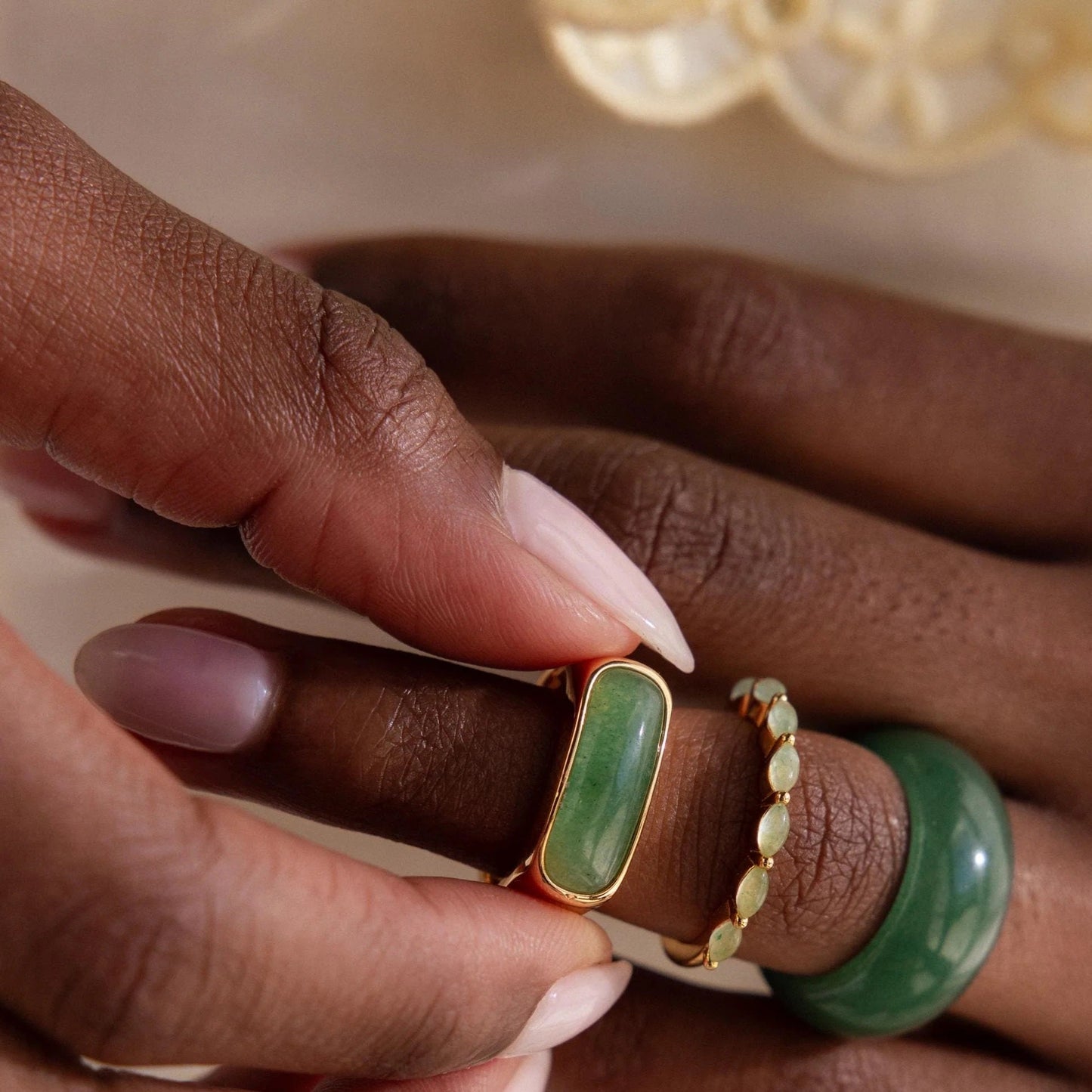 Close-up of a hand wearing green and gold rings with a blurred background