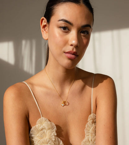 Woman wearing a beige floral dress with thin straps and a gold necklace, standing against a neutral background.
