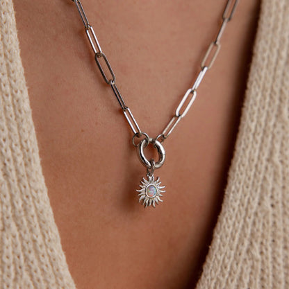 Silver necklace with a sun-shaped pendant on a person wearing a beige sweater.