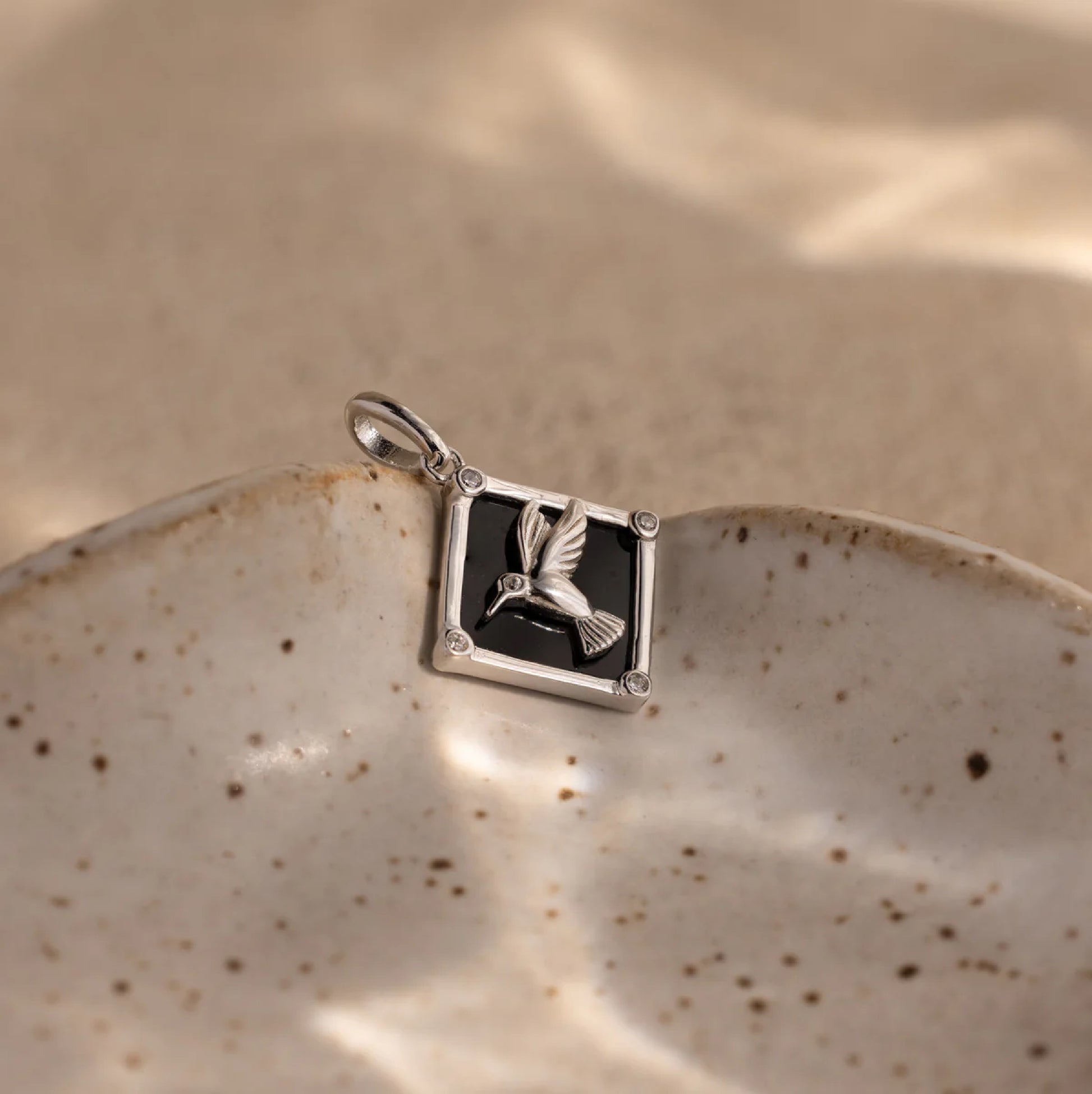 Silver pendant with a black stone and bird design on a ceramic plate