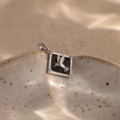 Silver pendant with a black stone and bird design on a ceramic plate