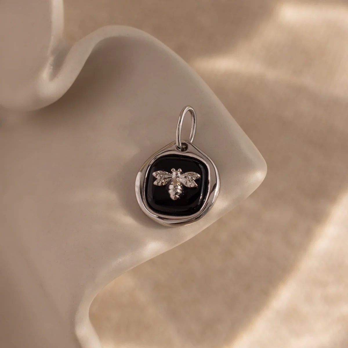Silver pendant with bee design on a beige stone surface