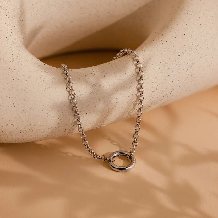 Silver chain necklace with a small ring pendant on a beige stone surface