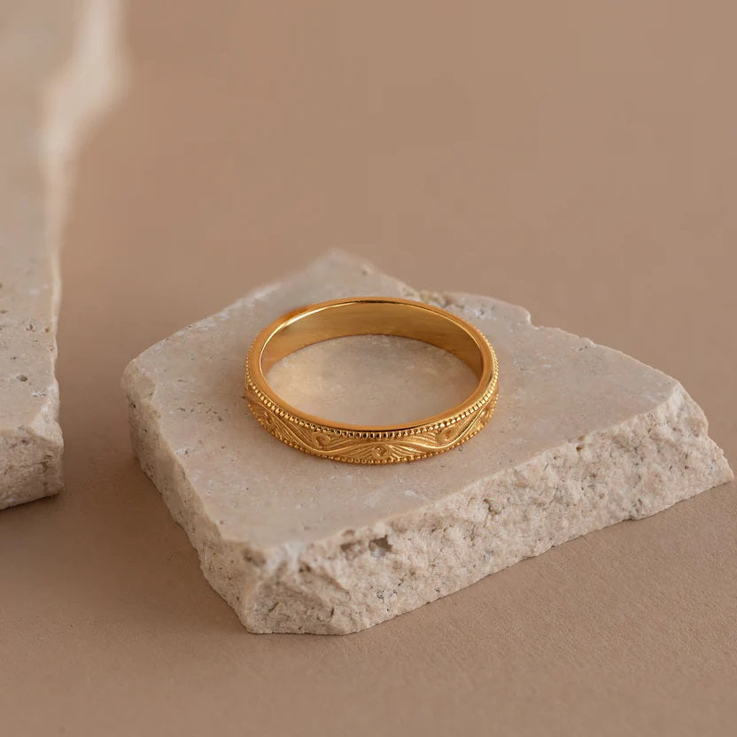 Gold ring with intricate design on a stone surface