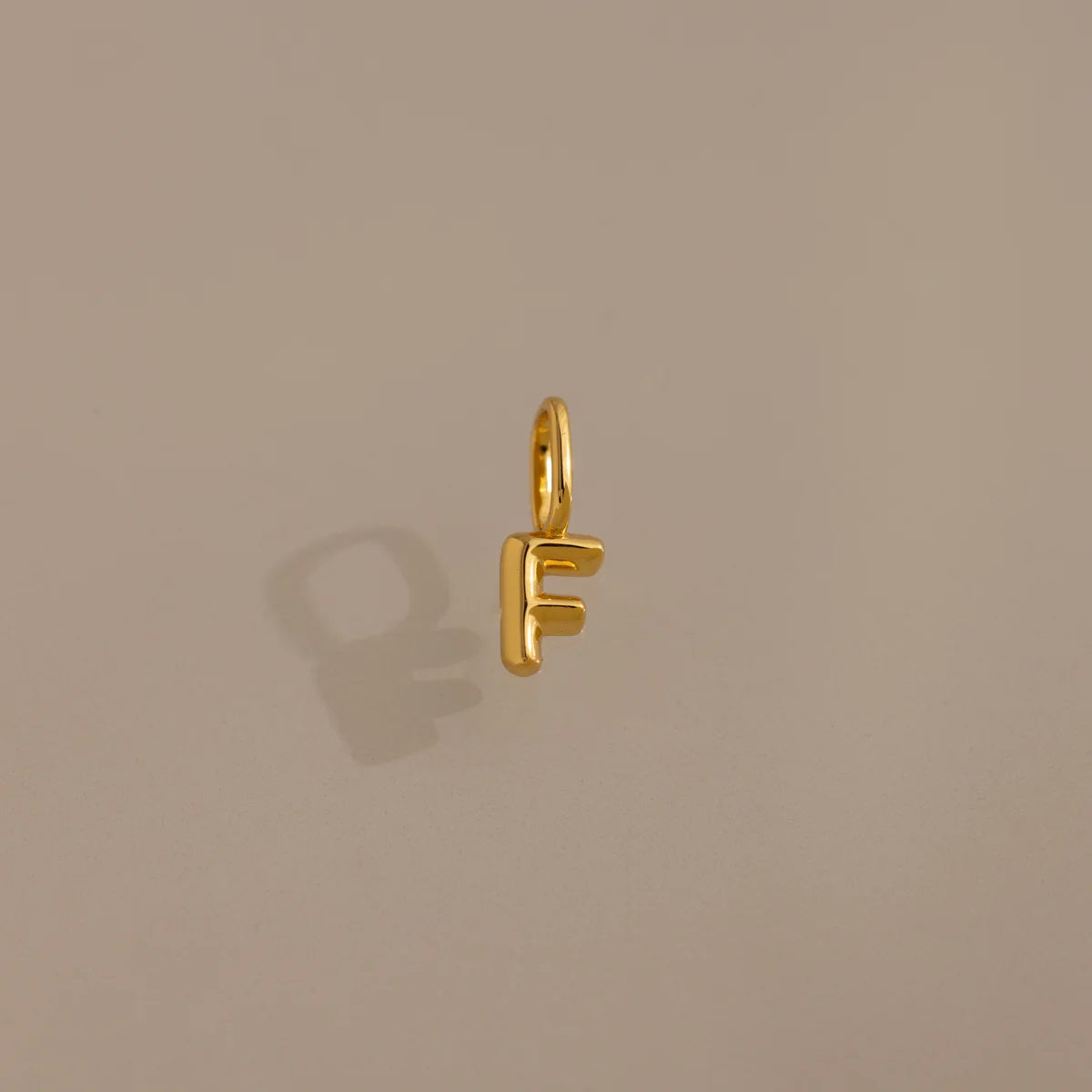 Gold letter 'F' charm on a beige background