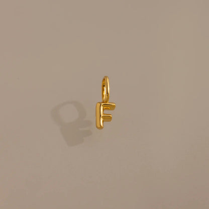 Gold letter 'F' charm on a beige background