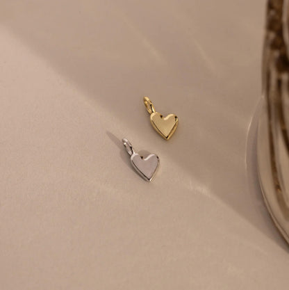 Two heart-shaped pendants, one gold and one silver, on a beige surface.