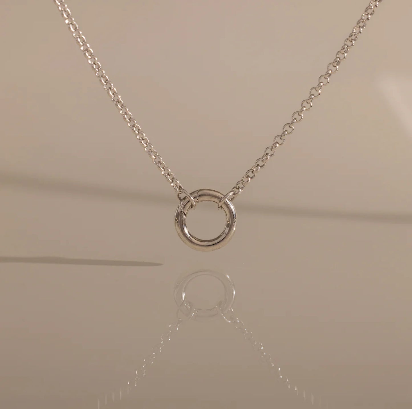 Silver necklace with a circular pendant on a beige background