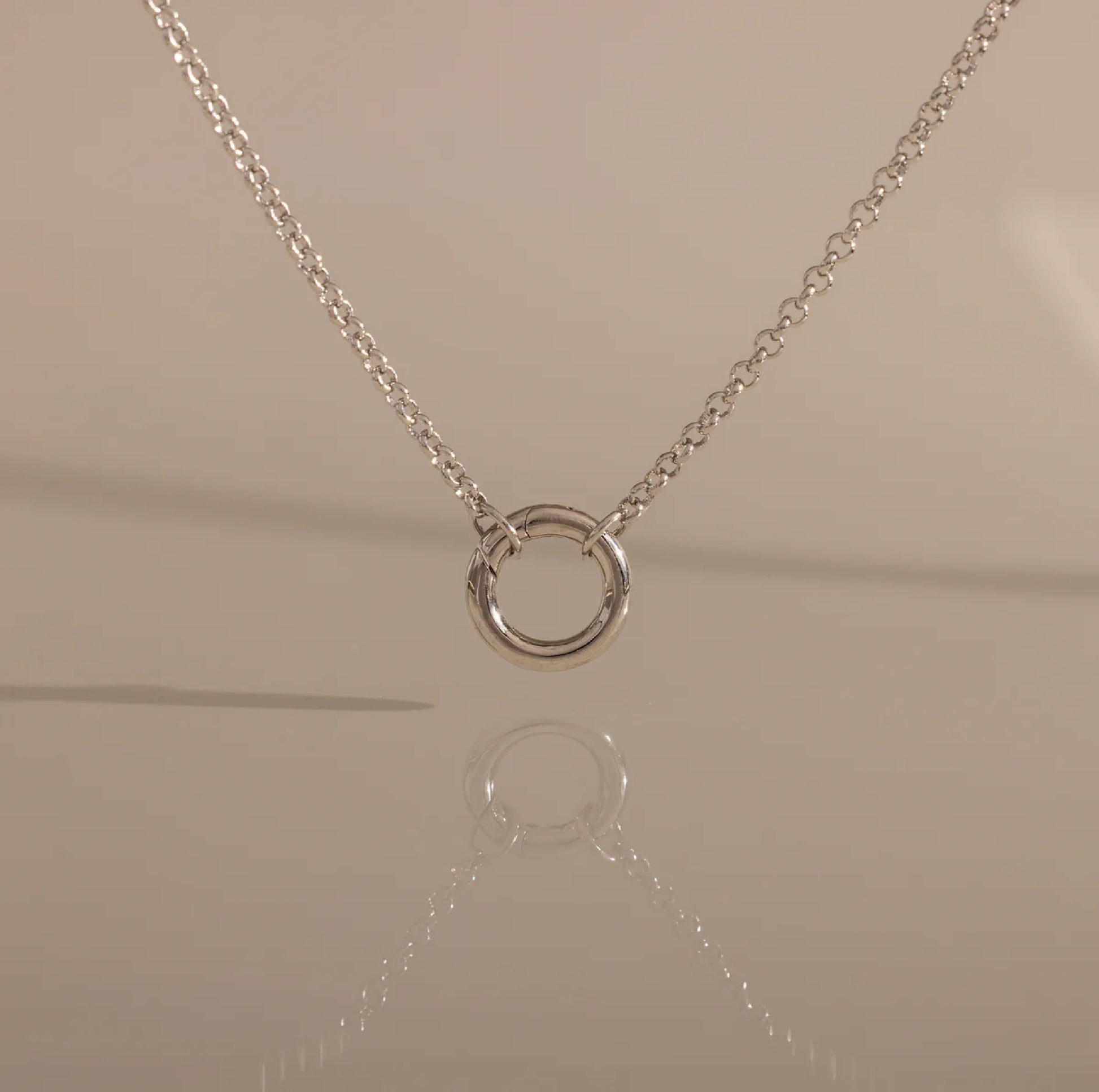 Silver necklace with a circular pendant on a beige background