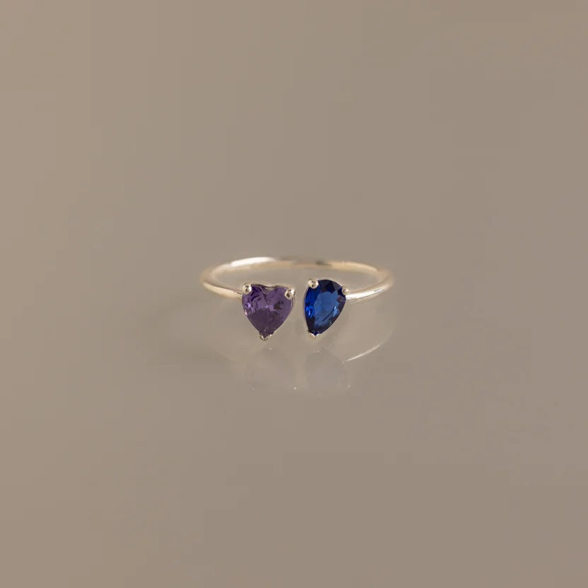 Silver ring with heart-shaped purple and blue gemstones on a beige background