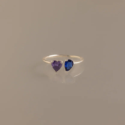 Silver ring with heart-shaped purple and blue gemstones on a beige background