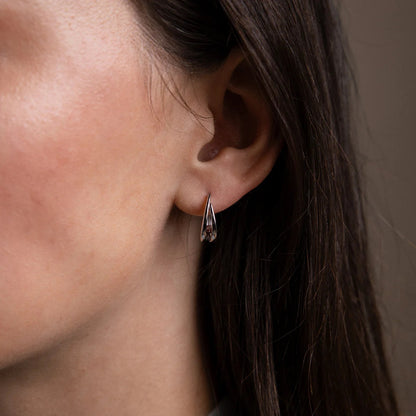 Close-up of a person wearing a silver earring with a neutral background