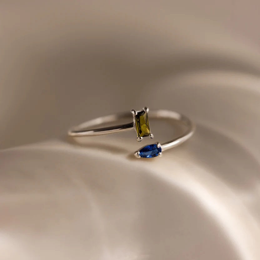 Silver ring with green and blue gemstones on a beige surface