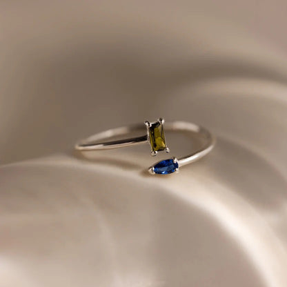 Silver ring with green and blue gemstones on a beige surface
