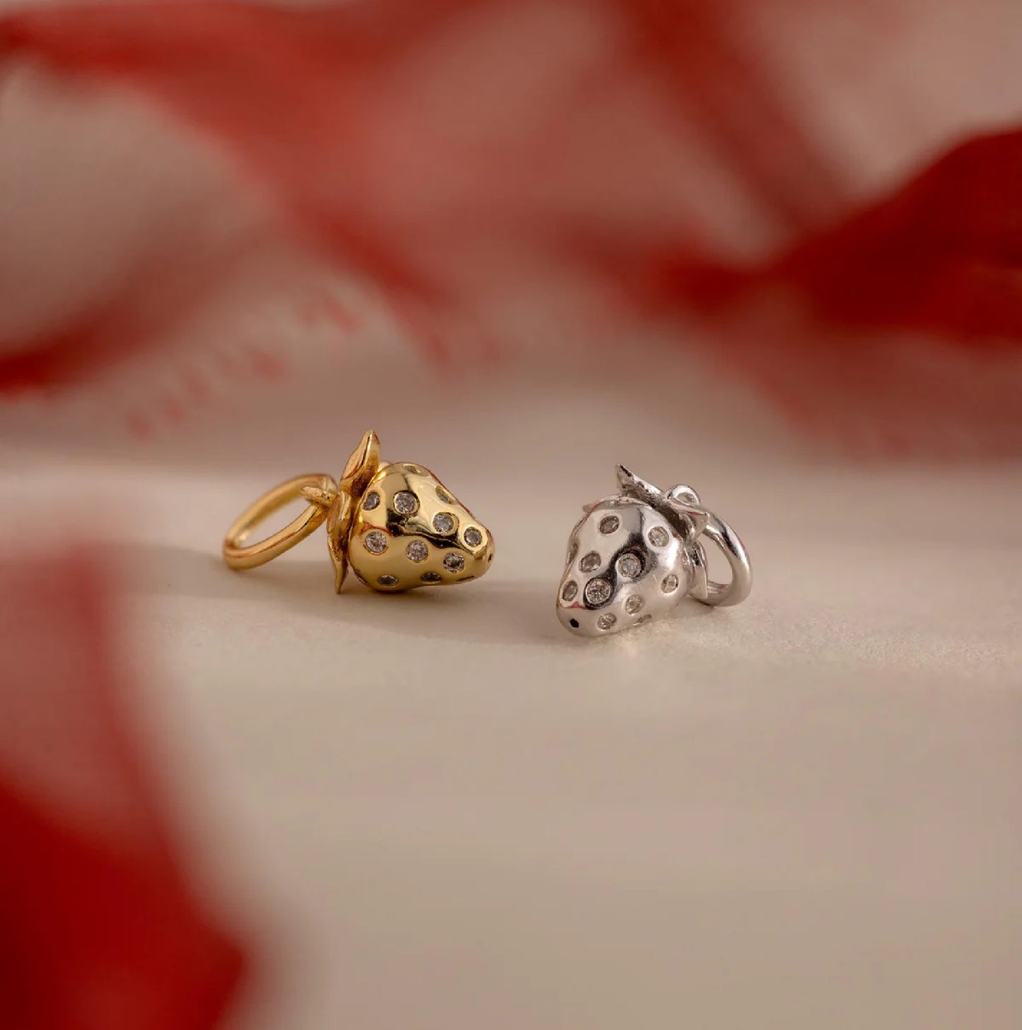 Gold and silver strawberry-shaped charms on a neutral background