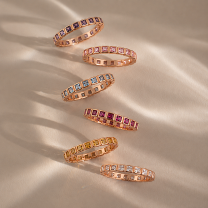 Set of rose gold eternity rings with various gemstones on a beige fabric background
