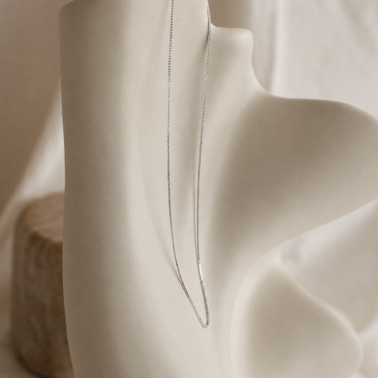 Close-up of a silver necklace draped over a white fabric surface