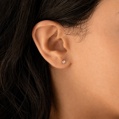 A close-up of a person's ear wearing a small round stud earring with a clear gemstone.