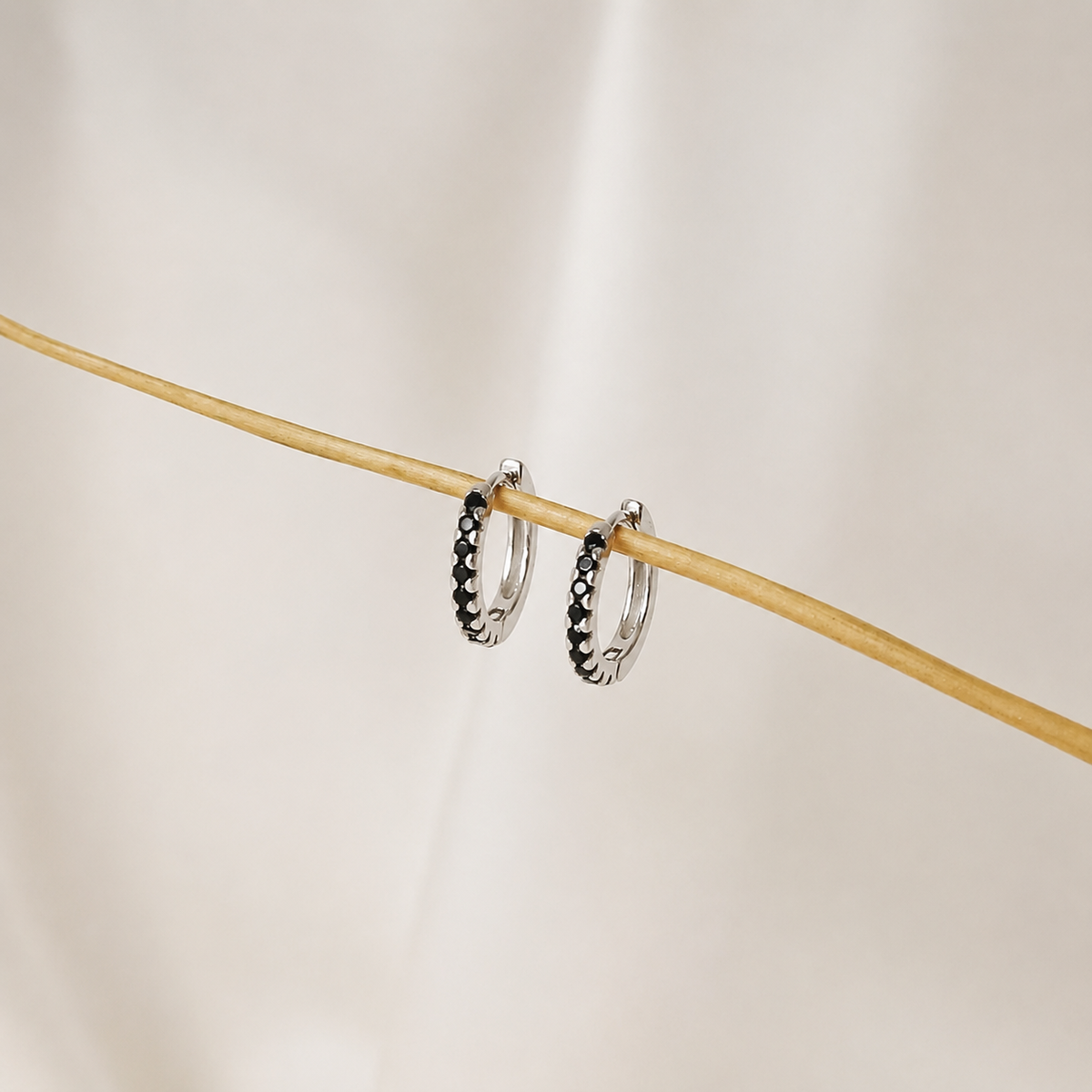 Two silver hoop earrings with black accents on a wooden stick against a neutral background
