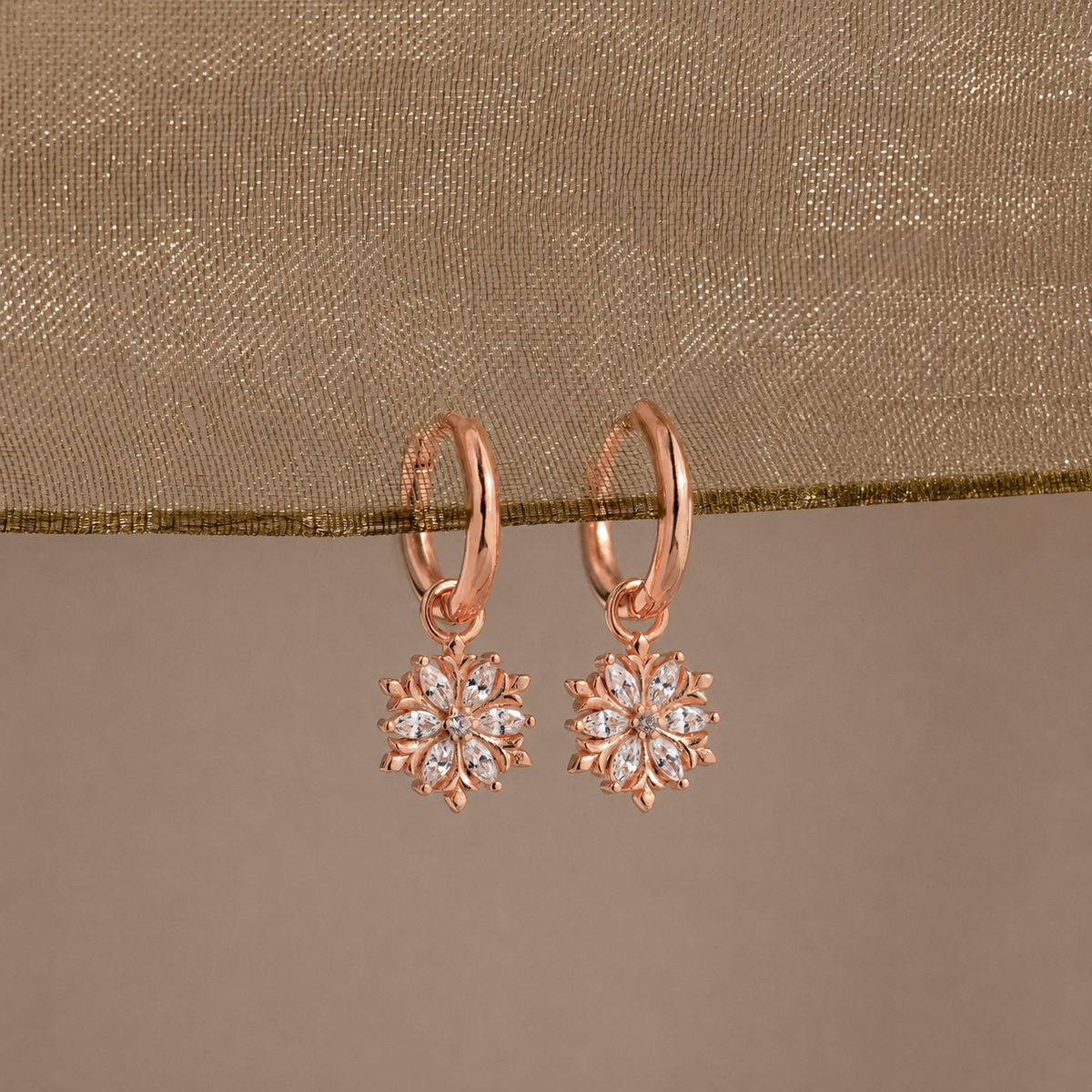 Rose gold earrings with diamond-like stones on a beige fabric background