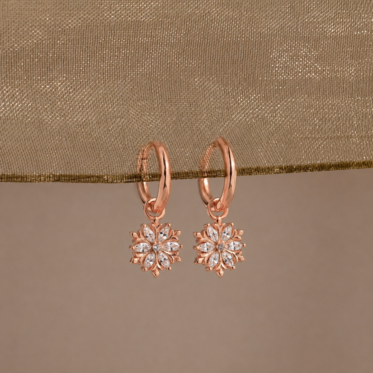 Rose gold earrings with diamond-like stones on a beige fabric background