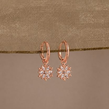 Rose gold earrings with diamond-like stones on a beige fabric background