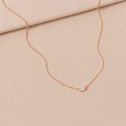 Rose gold necklace with a small rectangular pendant on a beige fabric background