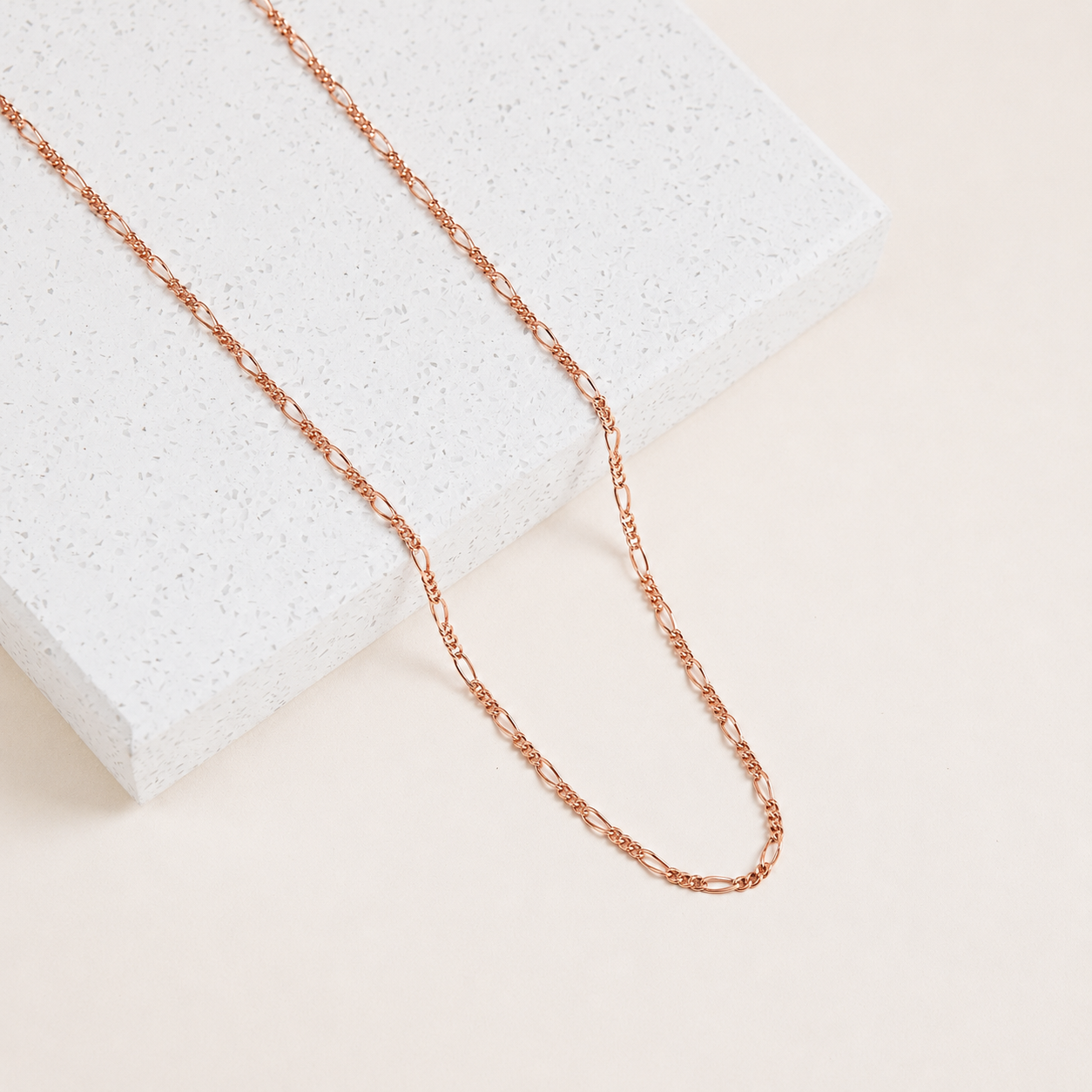 Rose gold chain necklace on a textured white surface