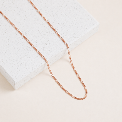 Rose gold chain necklace on a textured white surface