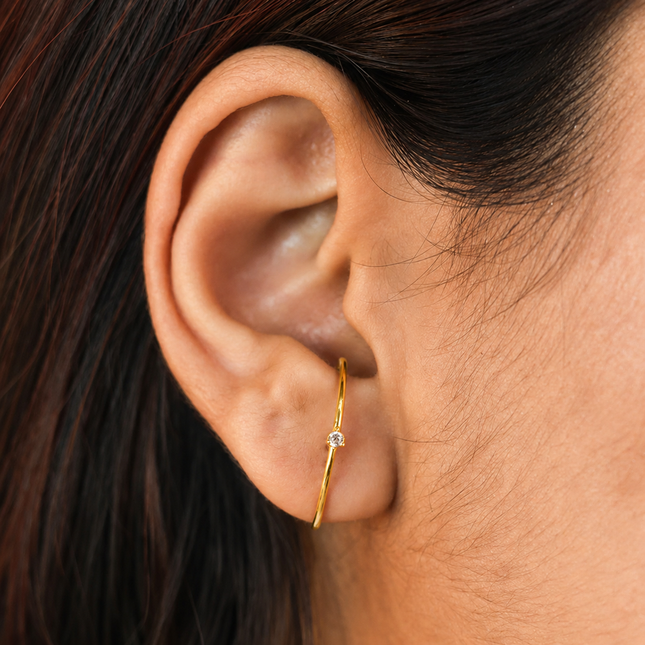 Close-up of an ear wearing a gold hoop earring with a small diamond.