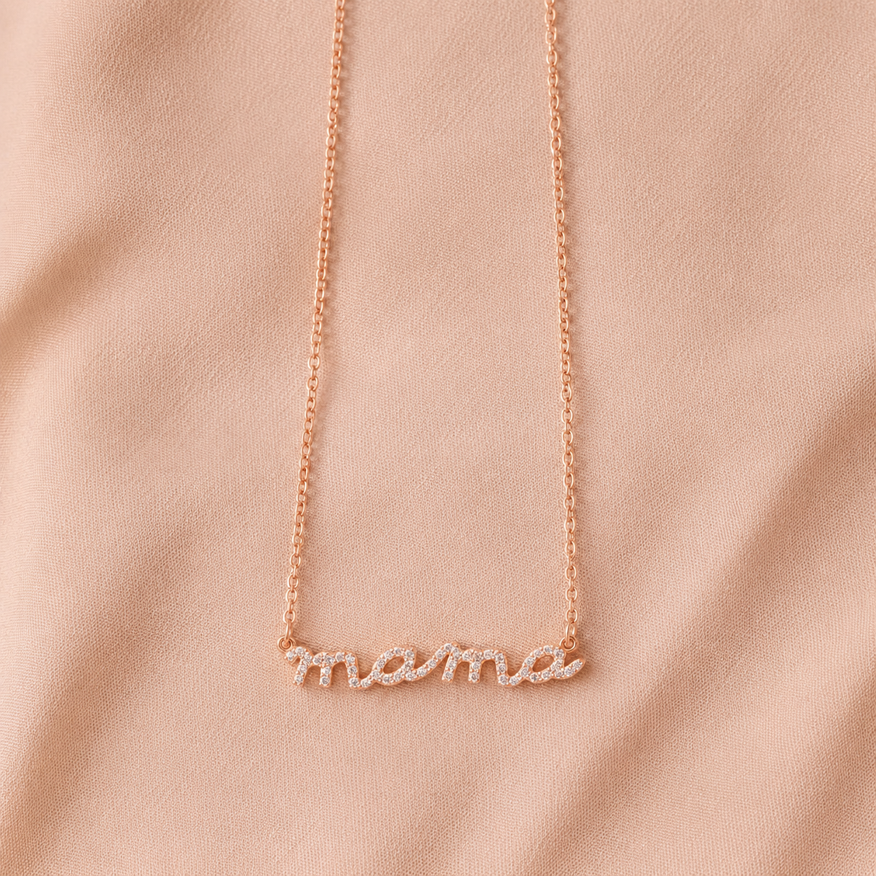 Rose gold 'mama' necklace on a pink fabric background