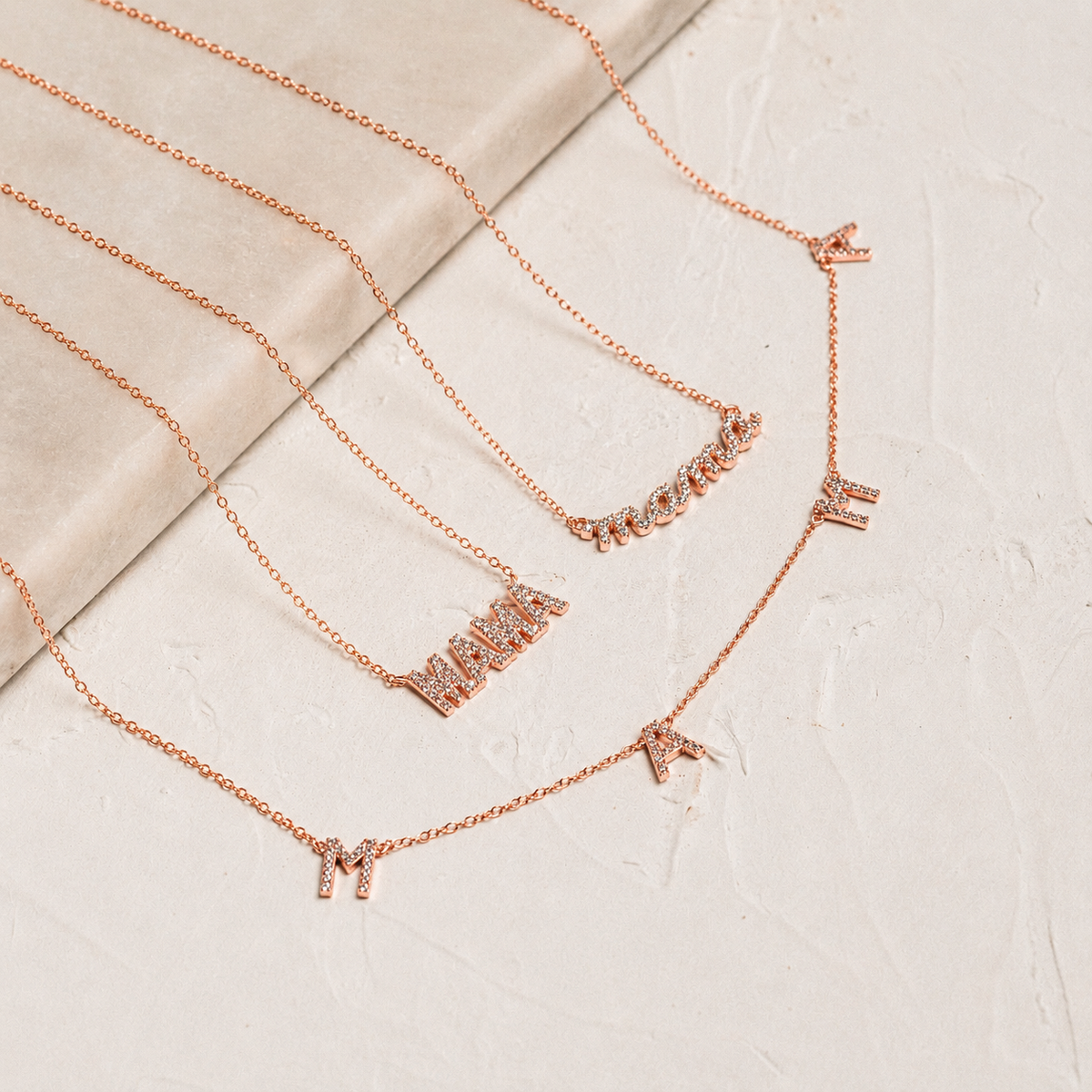 Set of rose gold necklaces with various pendants on a textured beige surface