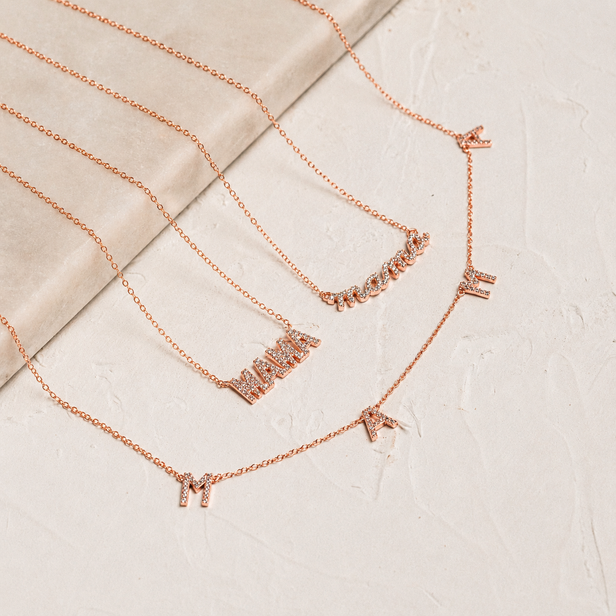Set of rose gold necklaces with various pendants on a textured beige surface