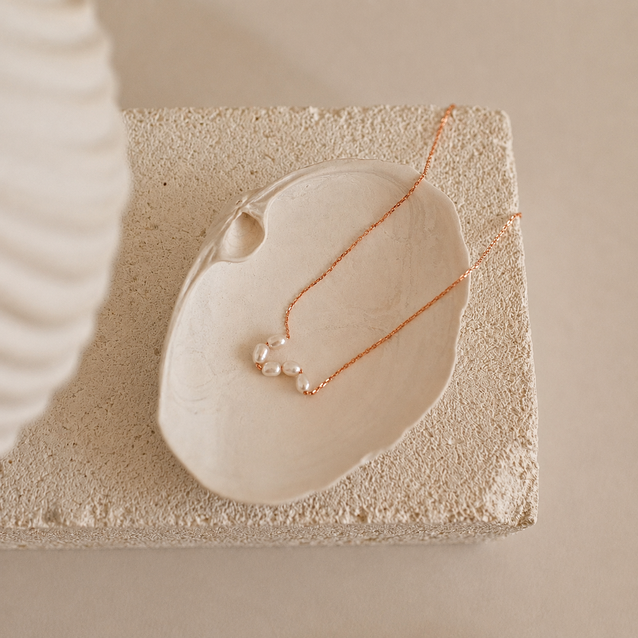 Rose gold necklace with pearl pendants on a textured stone surface