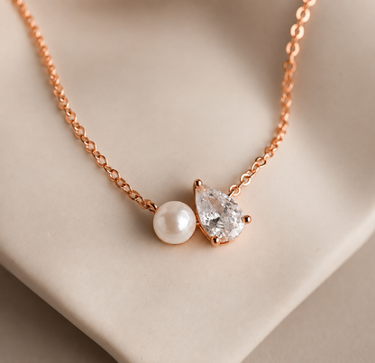 Necklace with a teardrop-shaped diamond and pearl pendant on a beige background