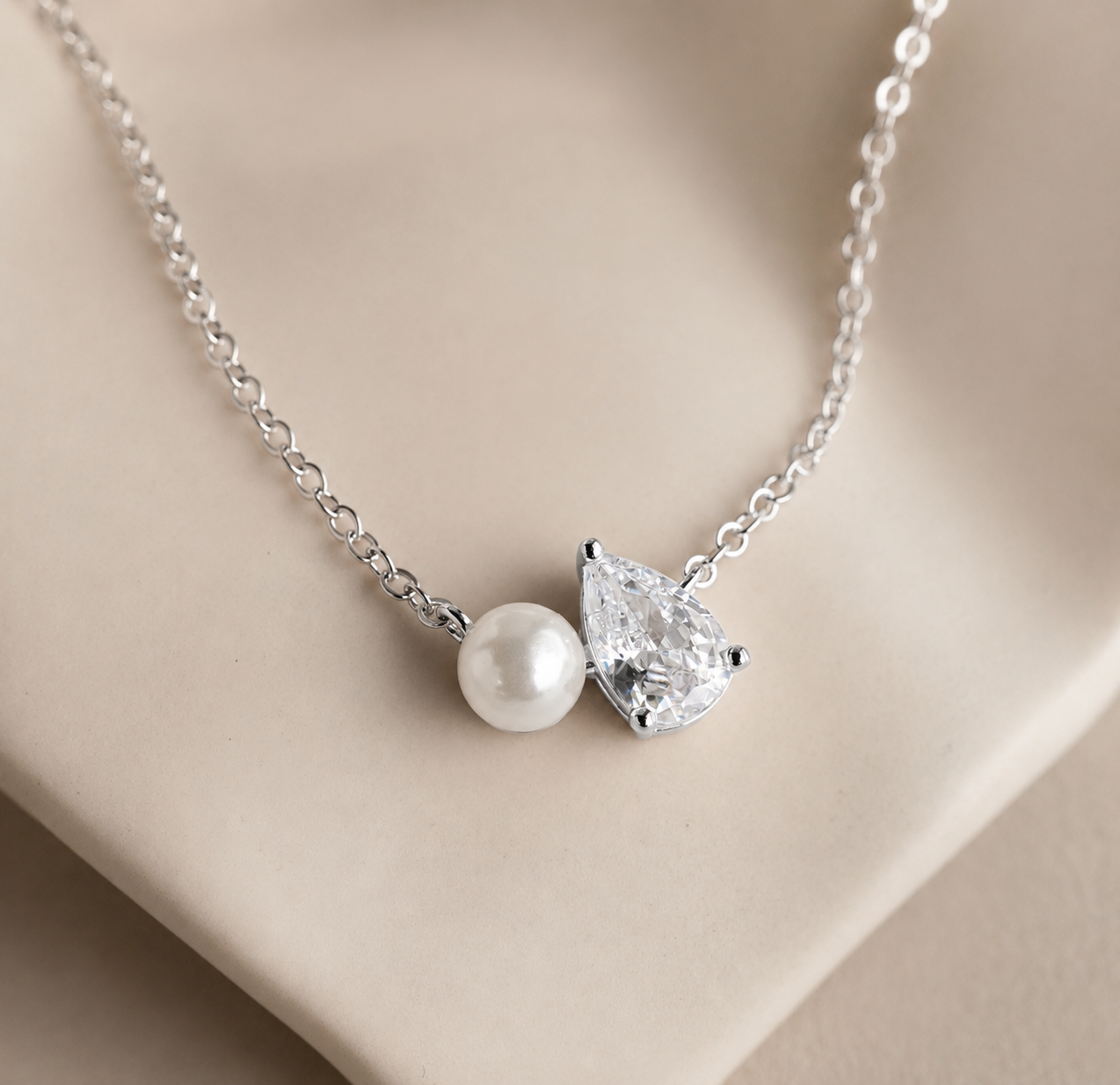 Necklace with a teardrop-shaped diamond and pearl pendant on a beige background