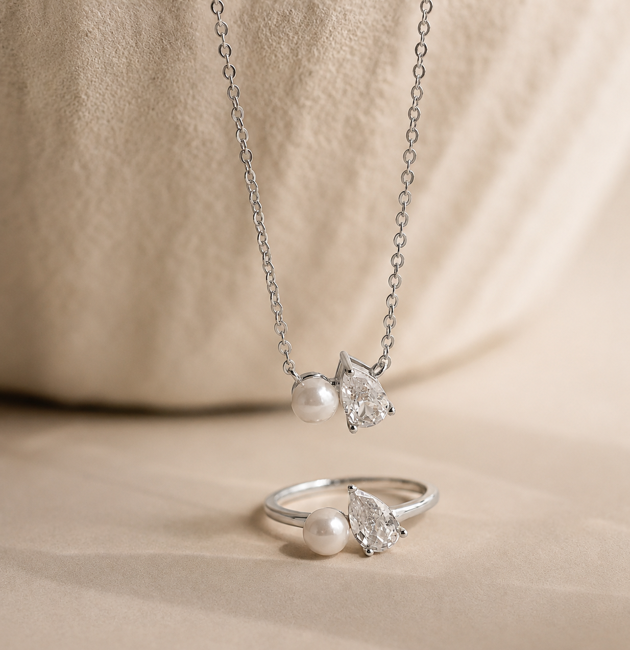 Silver necklace and ring set with pearls and gemstones on a beige fabric background