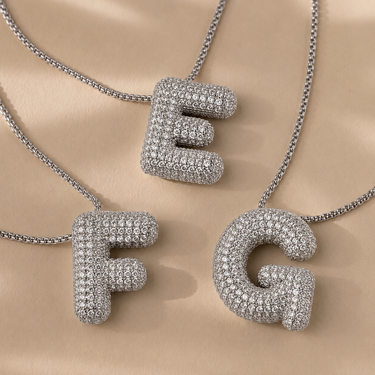 Silver letter pendants 'E', 'F', and 'G' on a beige background
