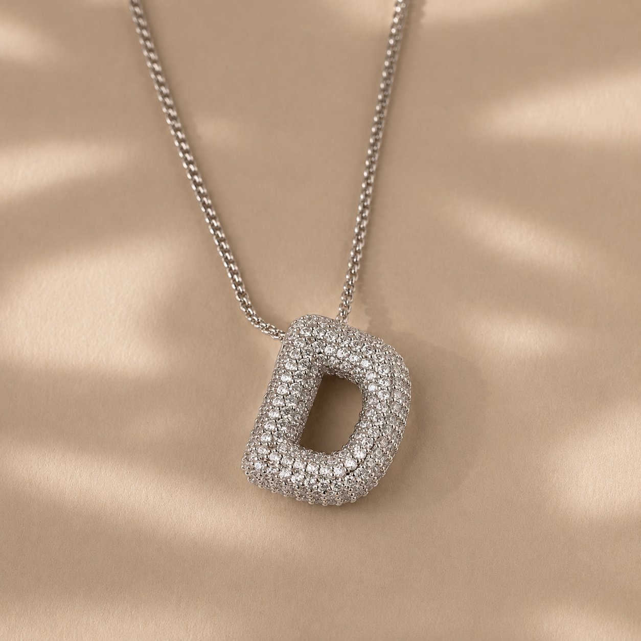 Silver necklace with a diamond-encrusted 'D' pendant on a beige background